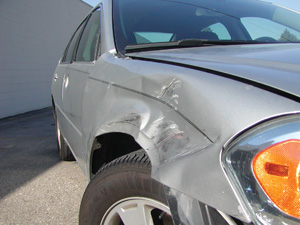 photo 6: side angle of a damaged fender to show the dent’s severity. the building behind the car provides a dark, simple background.